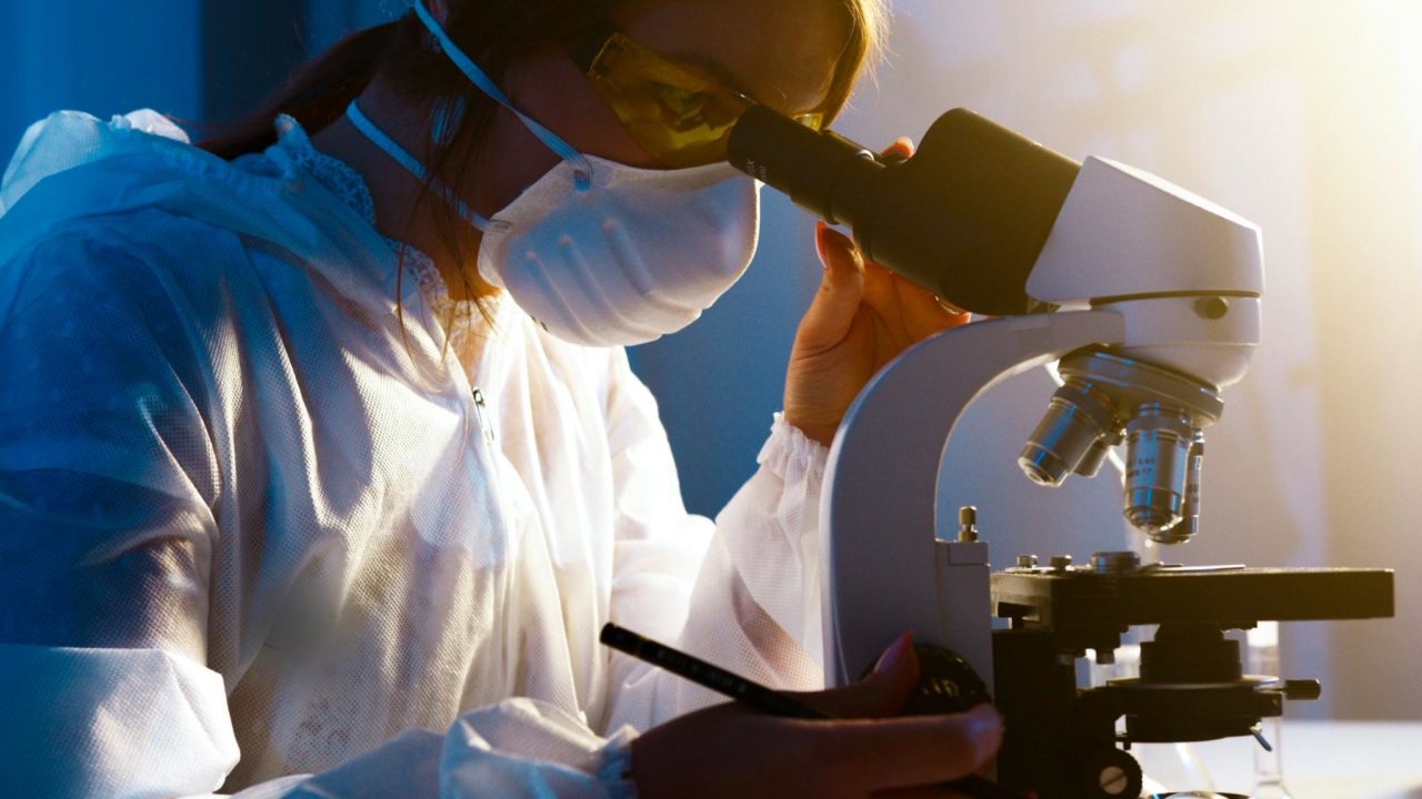 A woman works in a lab, looking into a microscope during her research.