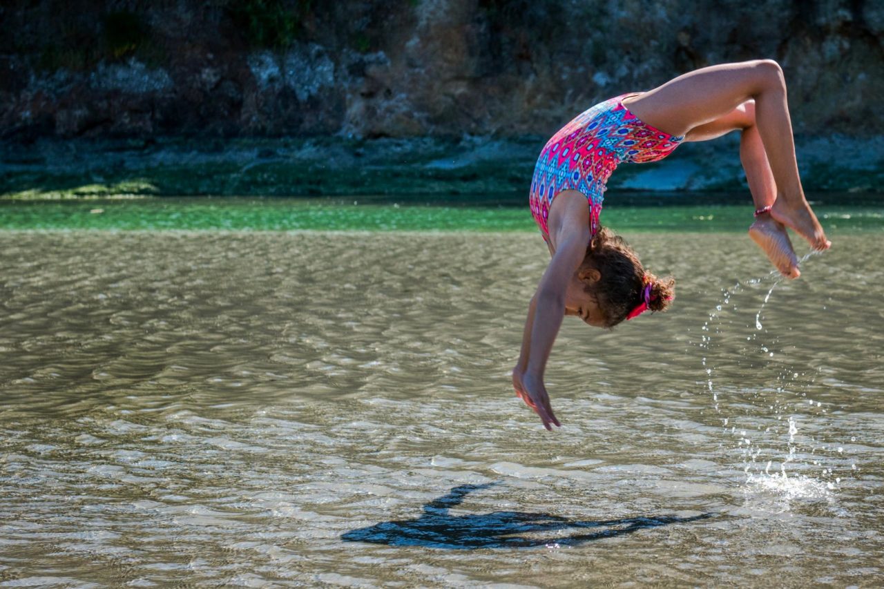 Una niña juega y realiza una voltereta en aguas poco profundas.