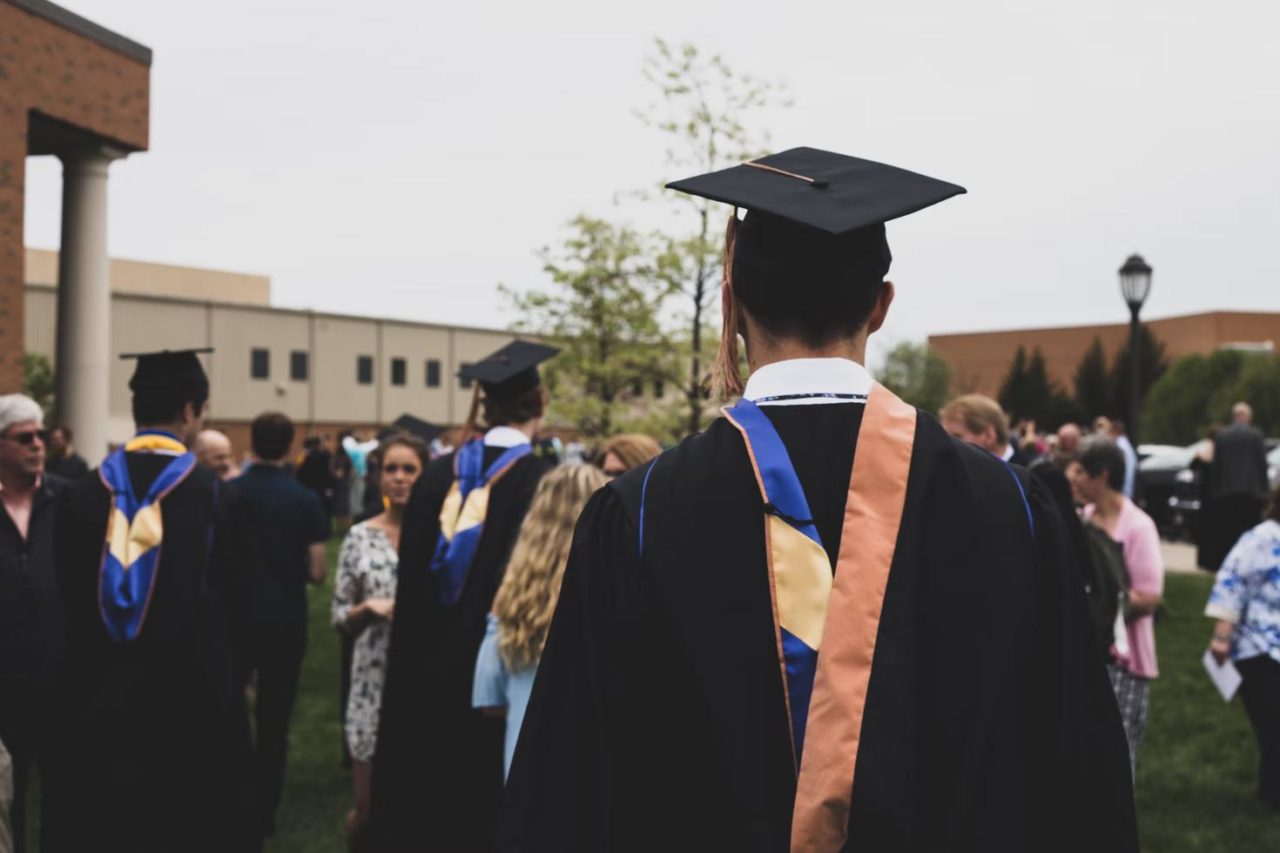 una ceremonia de graduación de la universidad con un estudiante con túnica de espaldas a la cámara.