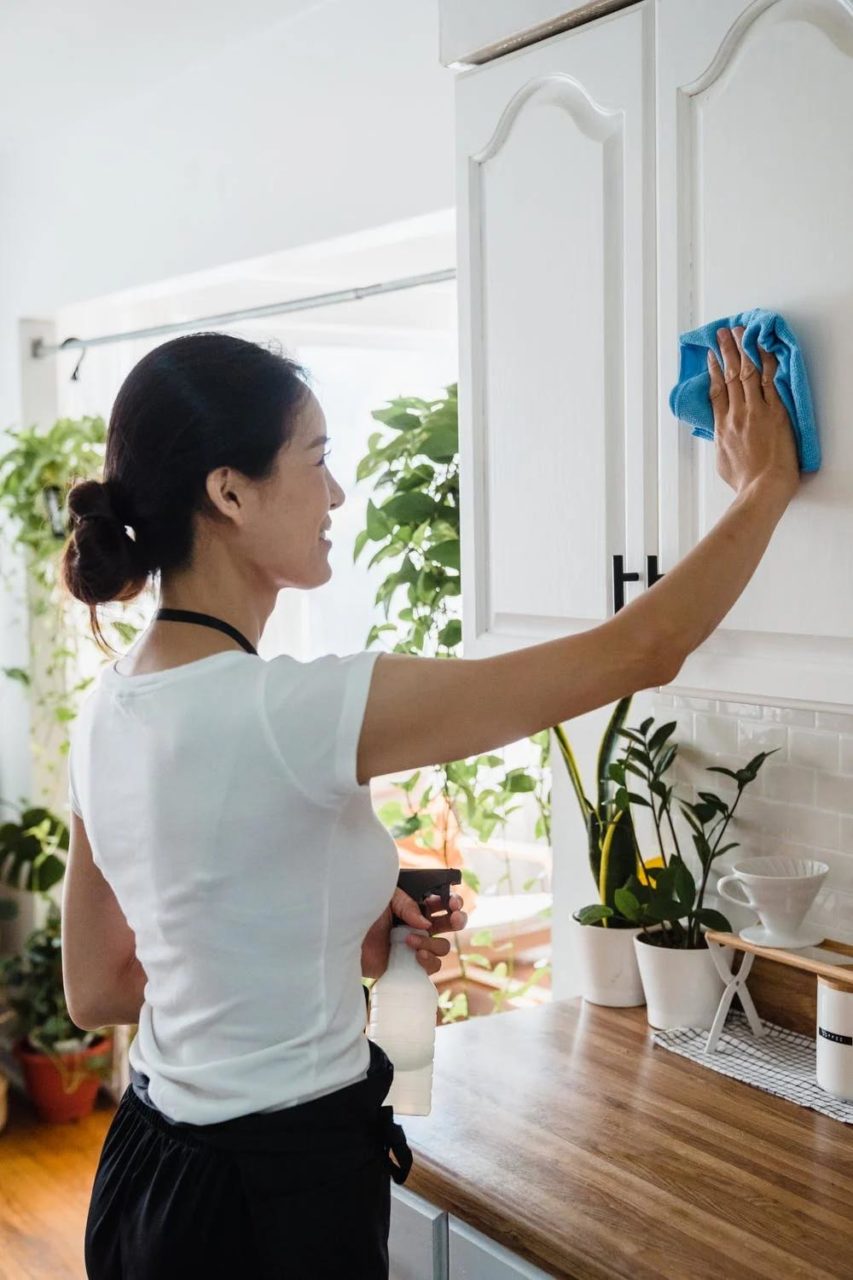A woman wipes down the cabinetry in her kitchen.