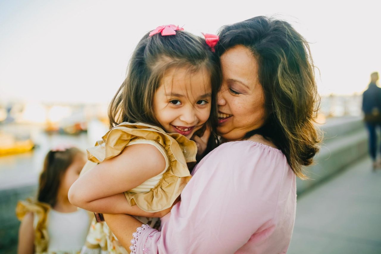 A mom and daughter hug affectionately, sharing smiles.