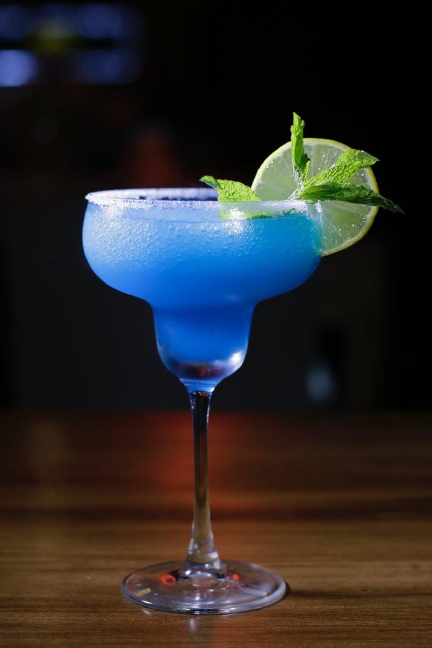 A fresh blueberry margarita with mint leaves and a lemon wedge on the edge.