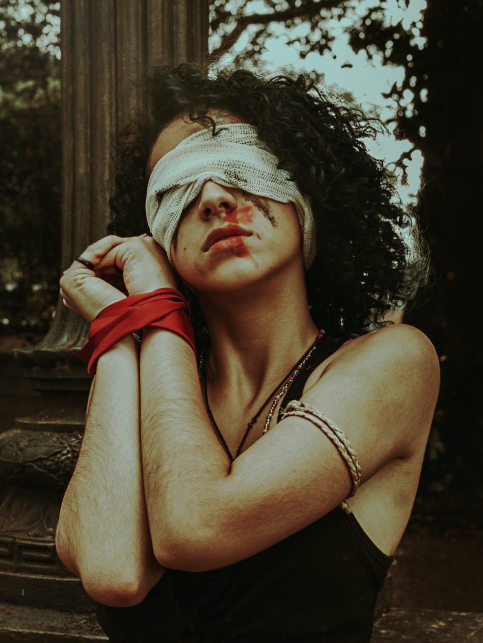 A woman with bloodstains on her mouth blindfolded with her hands tied.