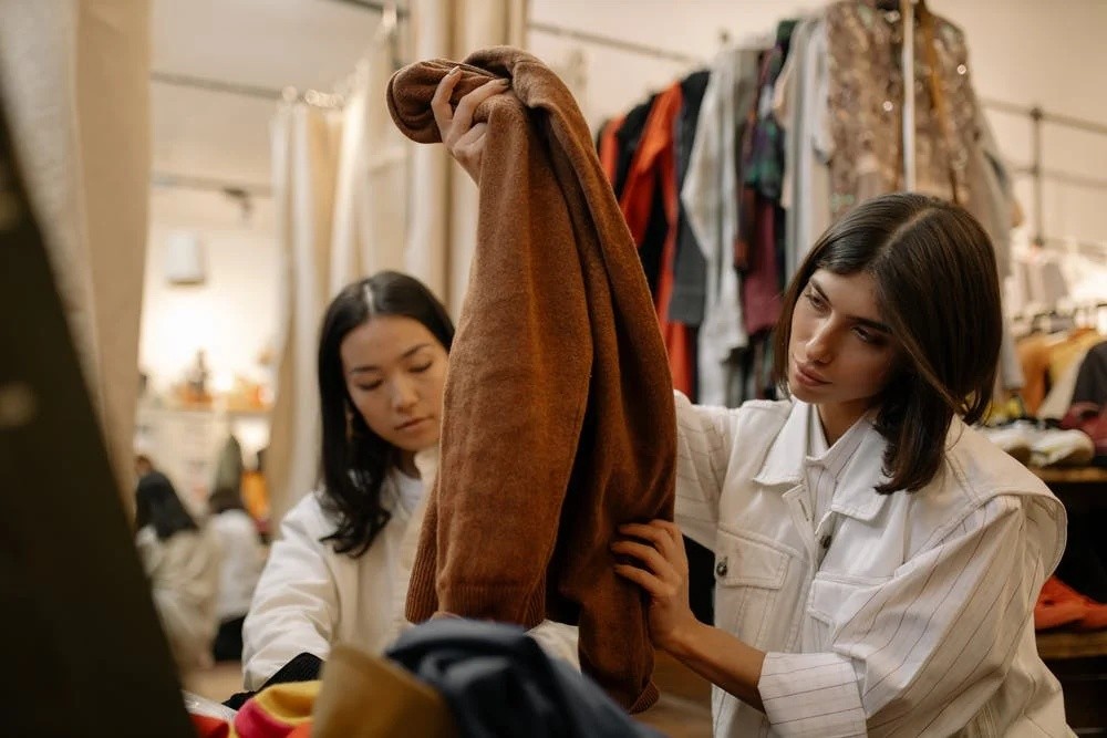 Two women pick out clothes from a pile in a thrift store.