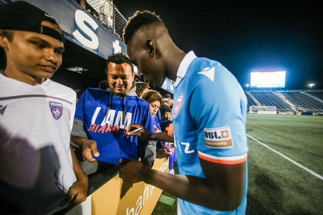 Jugador de Miami FC dando autógrafos en la camiseta de un aficionado.