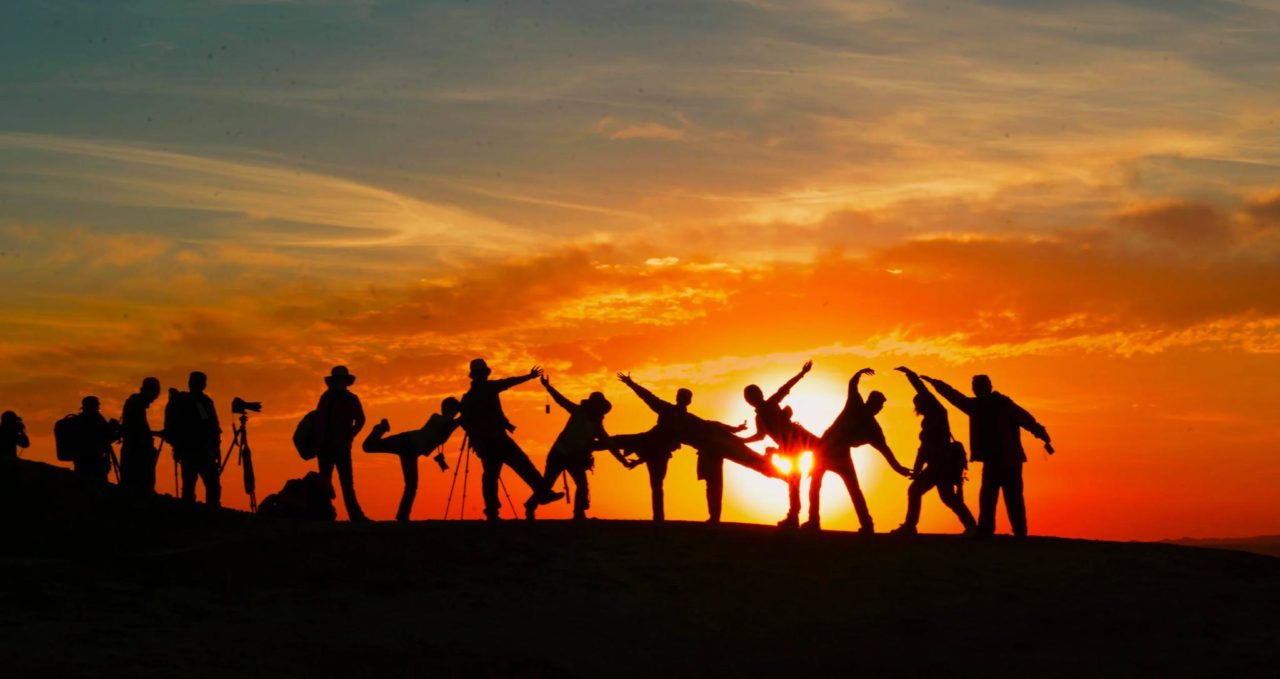 A group of people holding different poses against a backlit sunset.