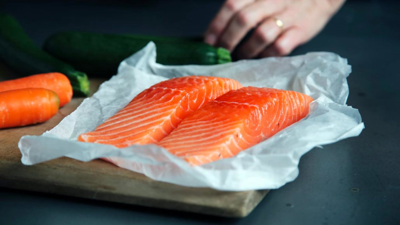 Two pieces of fresh salmon placed on parchment paper and a chopping board.