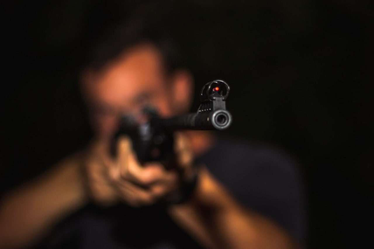 A person holds a gun, aiming it at something in the distance.