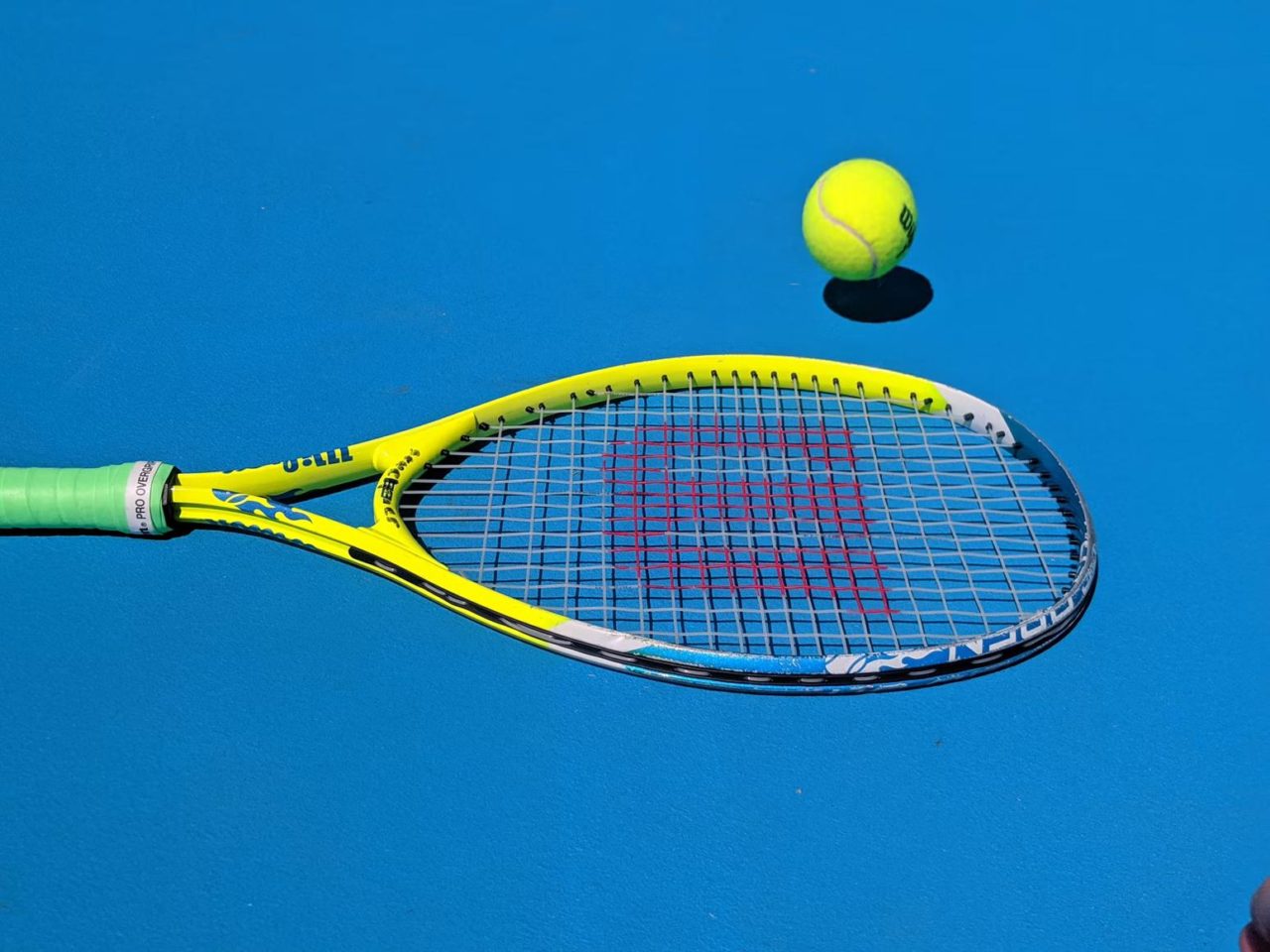 A tennis ball and racquet are placed on a blue tennis court.
