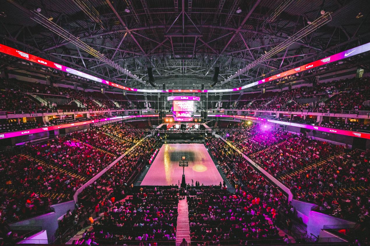 A basketball court in a stadium that is packed with thousands of audience members.