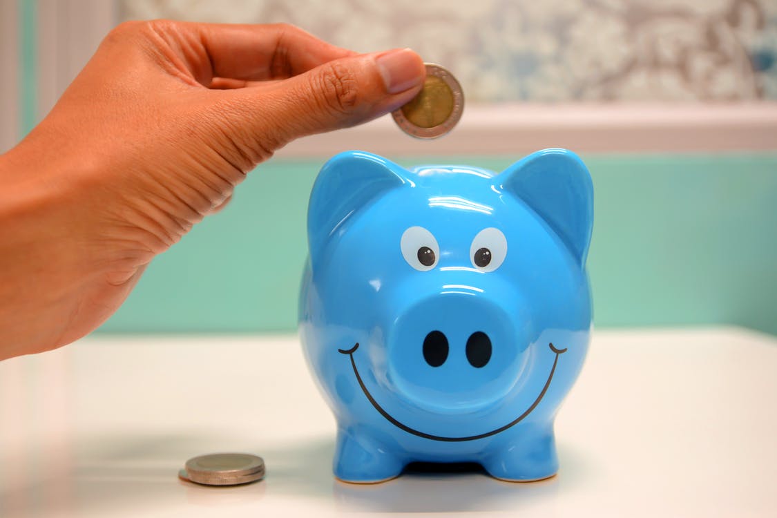 A person putting coins into a blue piggy bank.