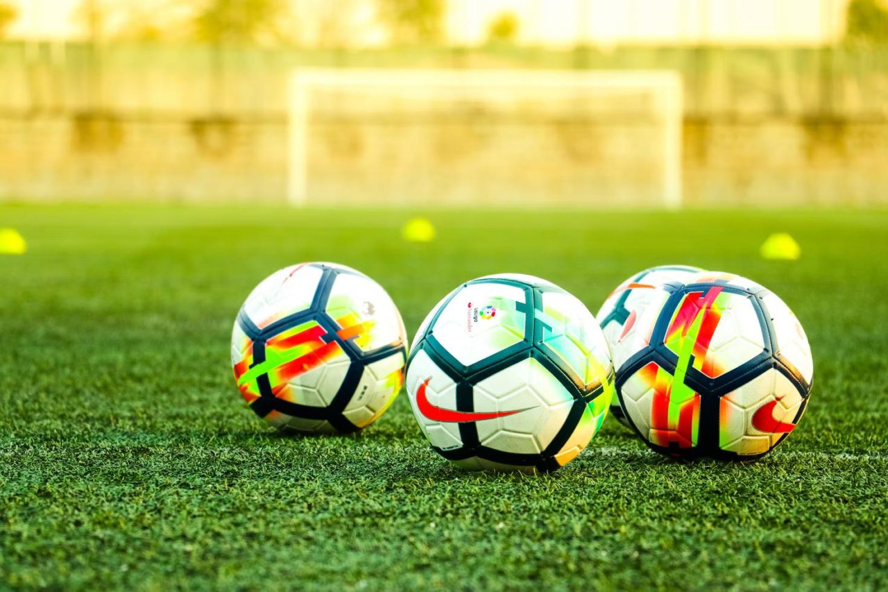 Three soccer balls are lined up on a field of grass.