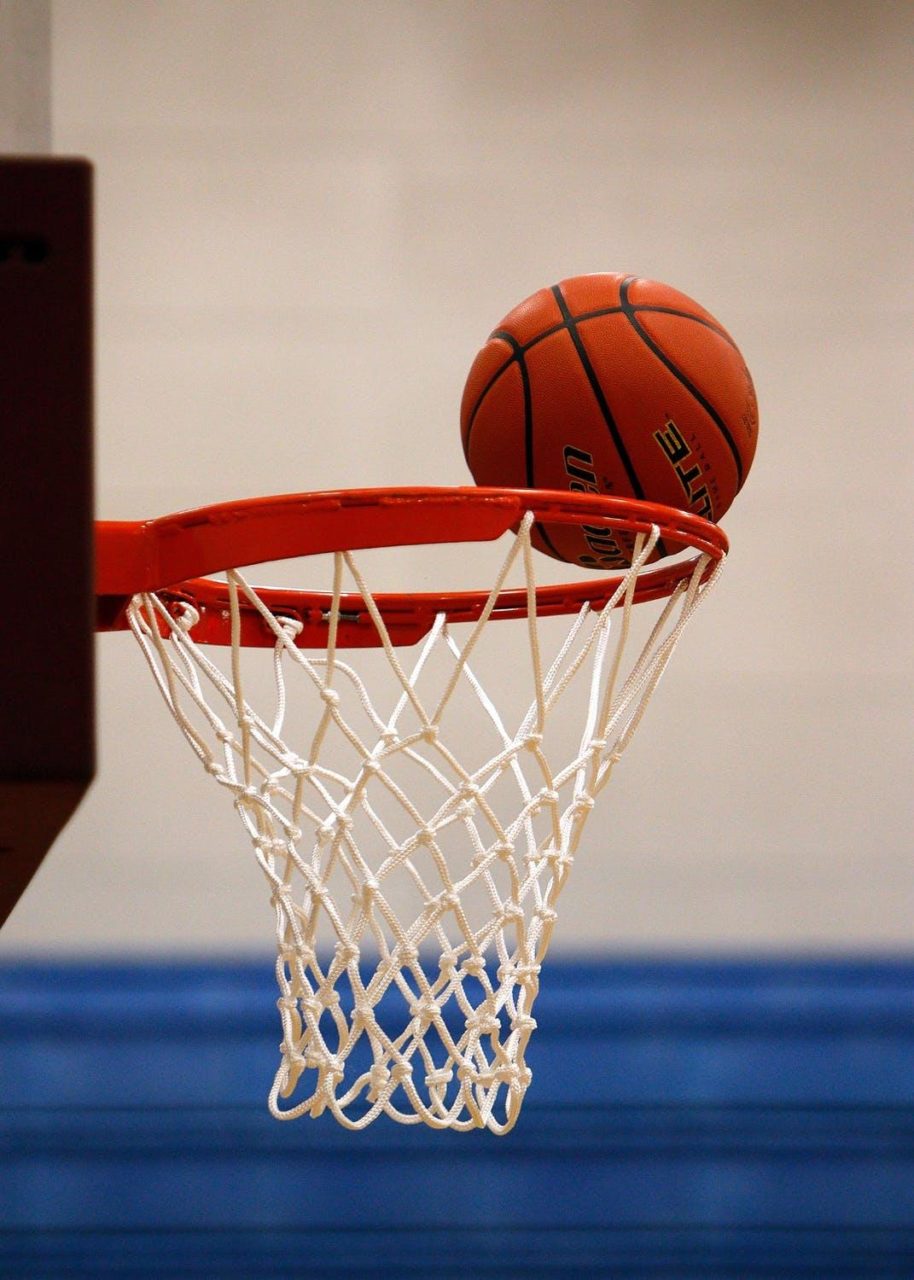 A basketball rests on a hoop during a game.