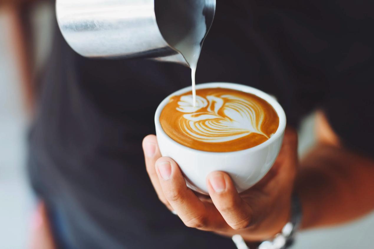 A barista makes a flower in a small latte cup.
