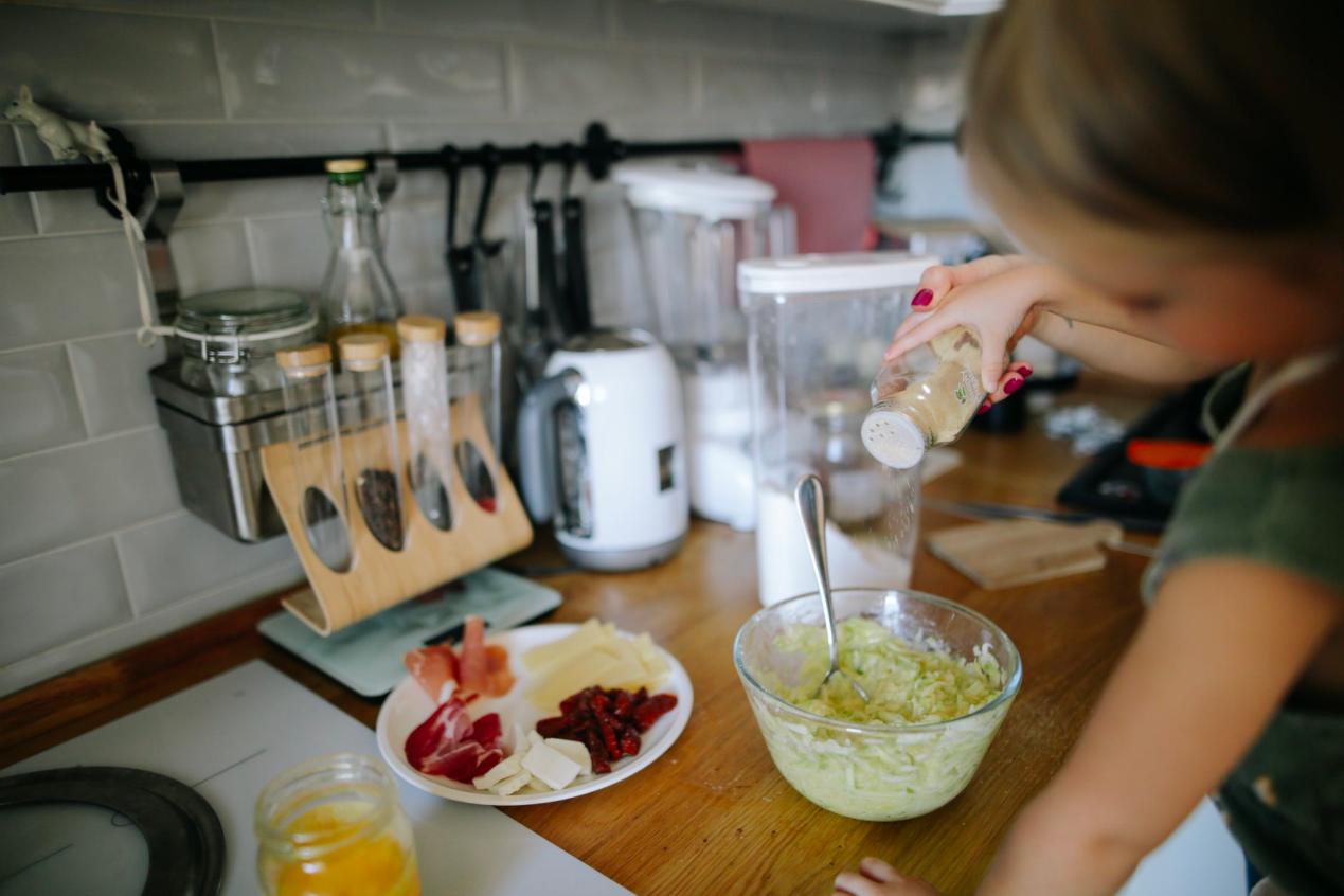 Una niña cocina mientras sazona una mezcla en un tazón.