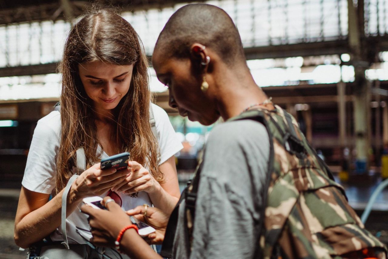 Dos turistas revisando sus teléfonos mientras están parados en una estación.