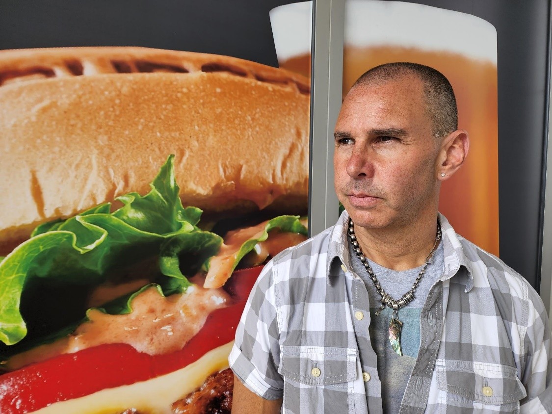 Jeffrey Hurwitt parado frente a un cartel de hamburguesas.