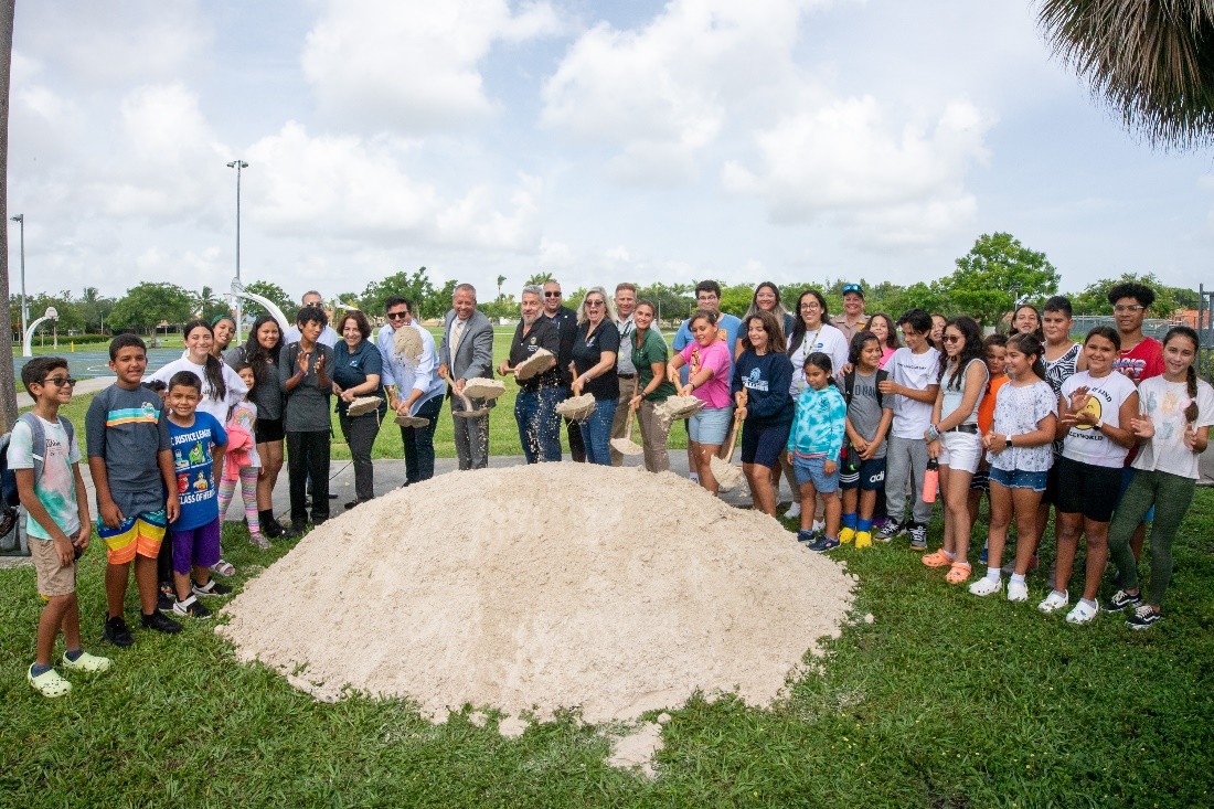 A group of people shovelling sand in a park.