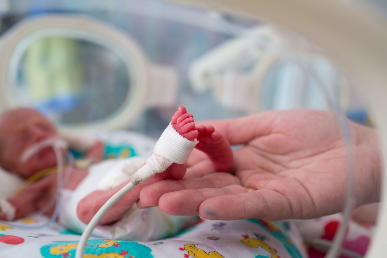 premature baby and close up of his feet in a humans hands