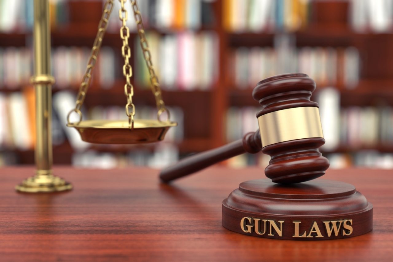 A gavel placed on a wooden stand with “gun laws” written on it