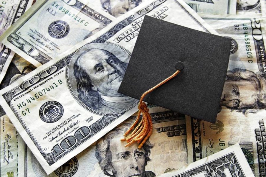 Dollar bills spread over with small graduation hat.