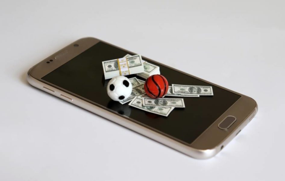 dinero en miniatura y una pelota de baloncesto y fútbol colocados en un teléfono