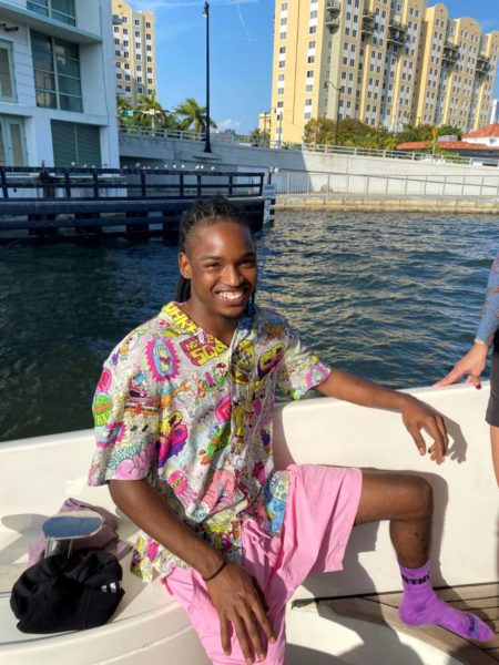 Enoch Tong con atuendo vibrante y calcetines rosas se sienta elegantemente en un barco