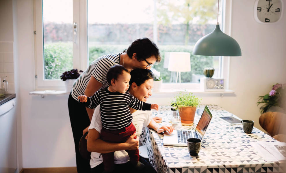 A family of three collaborating on a laptop in the kitchen, engaged in a productive and harmonious atmosphere.