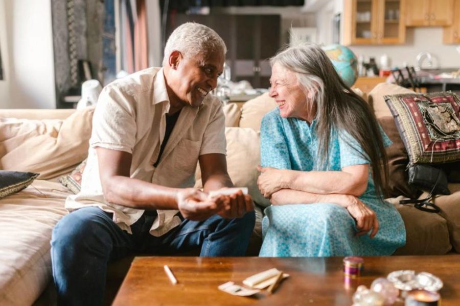 An older couple smiles while rolling marijuana joints.