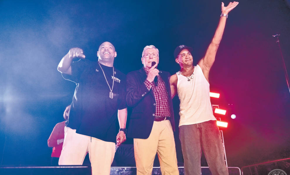 A man standing in front of a brightly lit carnival at night, filled with colorful rides and bustling crowds.