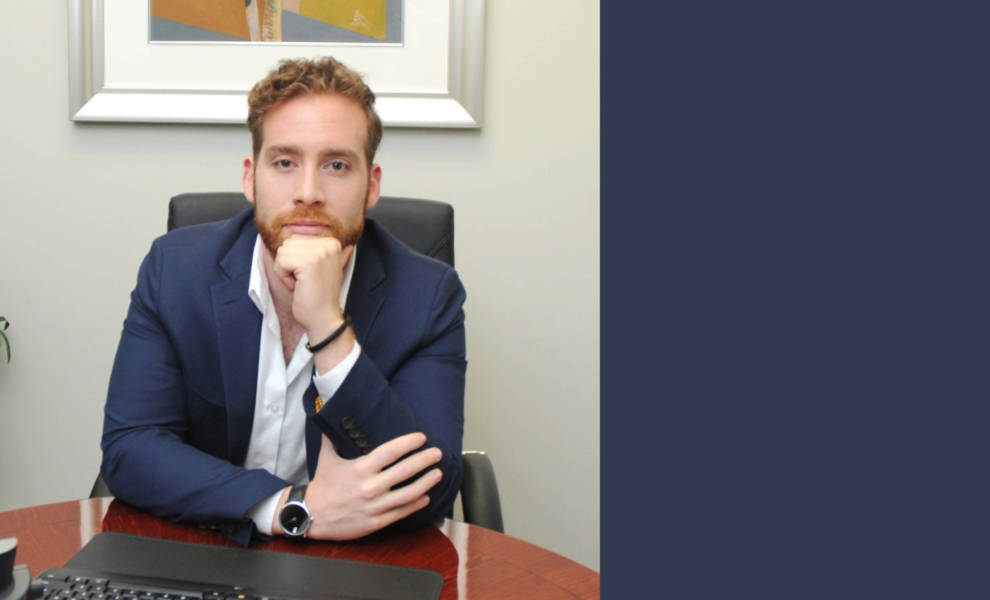 Un hombre de traje sentado pensativamente en un escritorio, con la mano apoyada en la barbilla, sumido en una profunda contemplación.