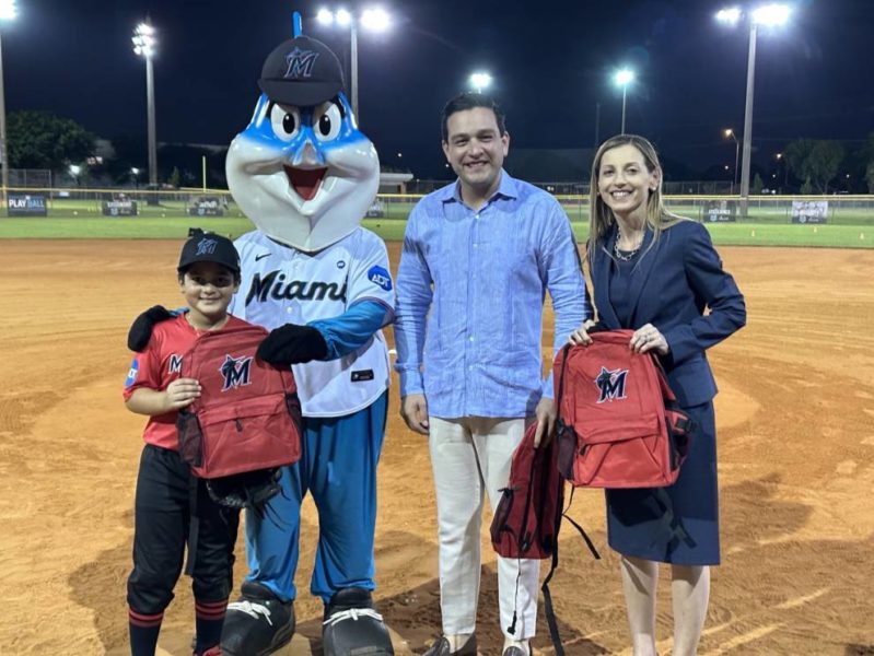 Two individuals and a mascot smiling for a photo on a baseball field, capturing a moment of camaraderie and team spirit.