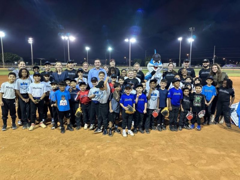 Un grupo de niños sonriendo y posando para una foto en un campo de béisbol, capturando su alegre camaradería.