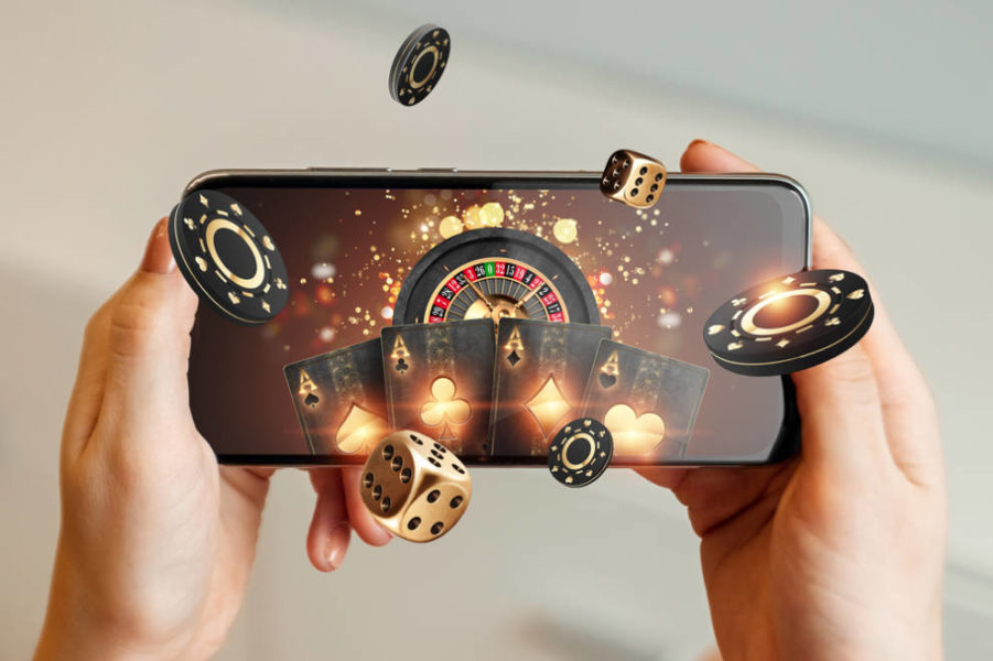 Dice and cards are coming out of a phone while a hand is holding them from underneath promoting online gaming