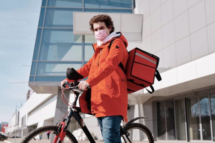 Delivery man wearing a face mask while riding a bicycle, representing a gig economy employee in the delivery sector.