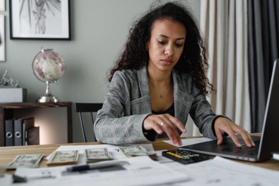 Woman in plaid blazer using laptop and mobile phone for tax filing with software applications in focus.