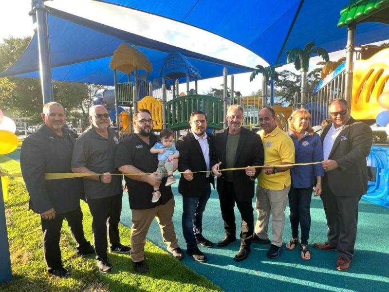 A group of people joyfully cutting the ribbon at a playground, celebrating its grand opening