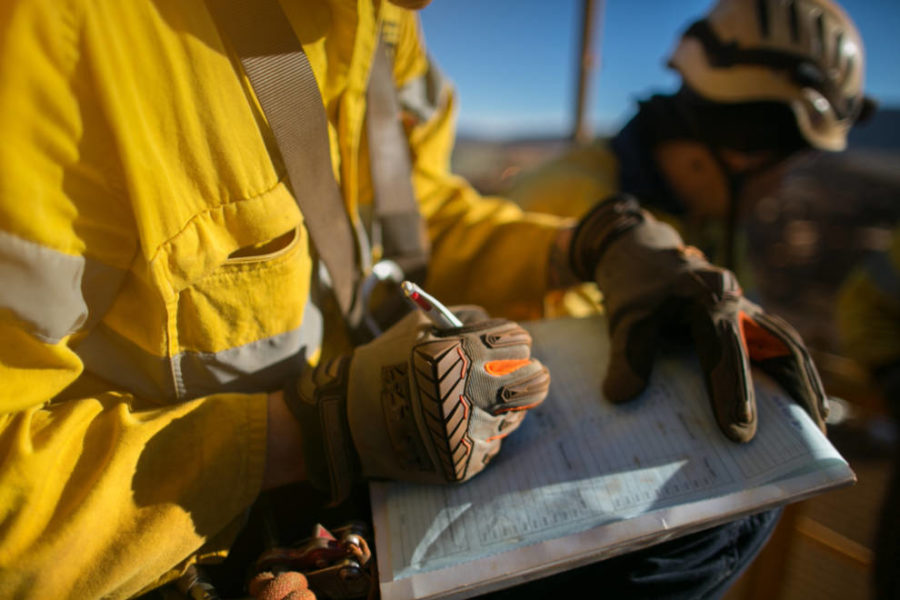 A man in yellow work clothes holds a clipboard, ready to record important information for his tasks