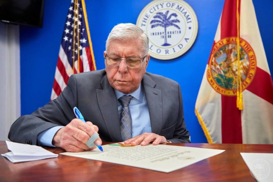 An elderly man in formal attire, seated at a desk, signing on a contract