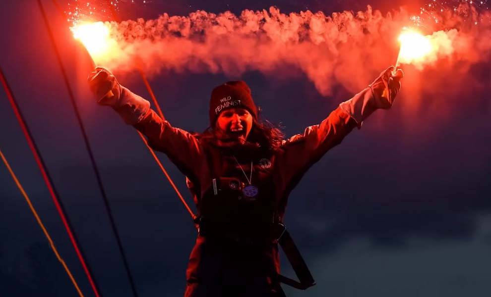 A sailboat gracefully sails in the ocean, with majestic mountains serving as a breathtaking backdrop.
