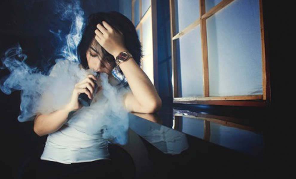 Mujer joven fumando un vaporizador en la oscuridad, que ilustra el uso de dispositivos de vapeo en ambientes con poca luz.