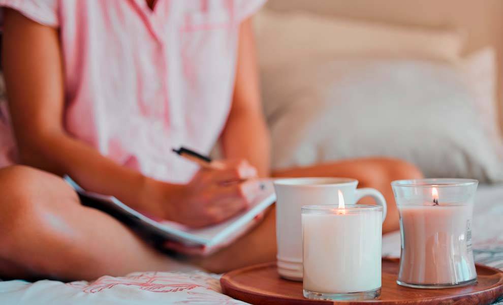 A woman sitting on a bed surrounded by candles and a notebook.