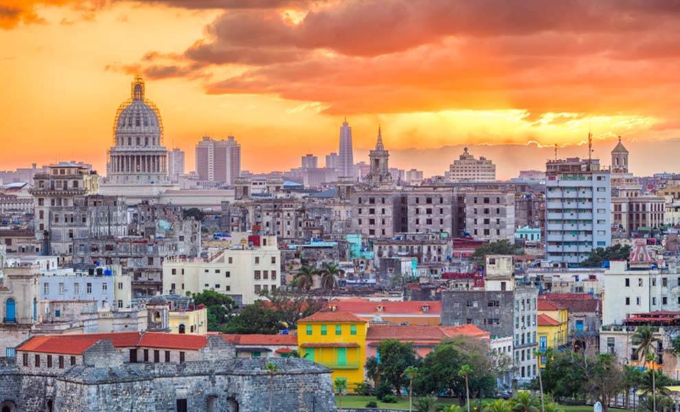 Una impresionante puesta de sol sobre la ciudad de La Habana, que proyecta un cálido resplandor sobre los coloridos edificios y palmeras.