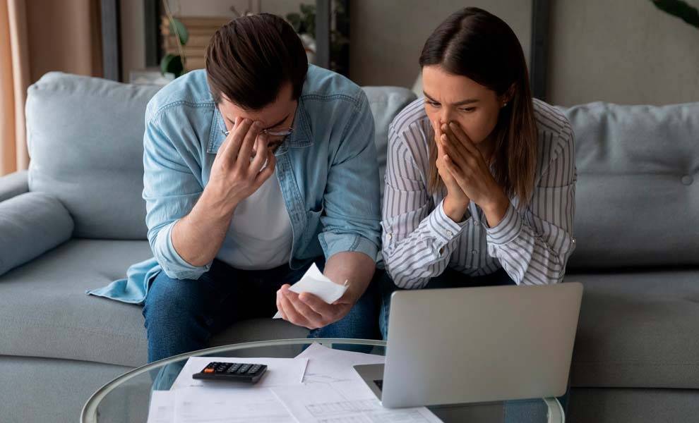 Una pareja sentada en un sofá, absorta en su computadora portátil y sus papeles, posiblemente discutiendo o trabajando juntos.