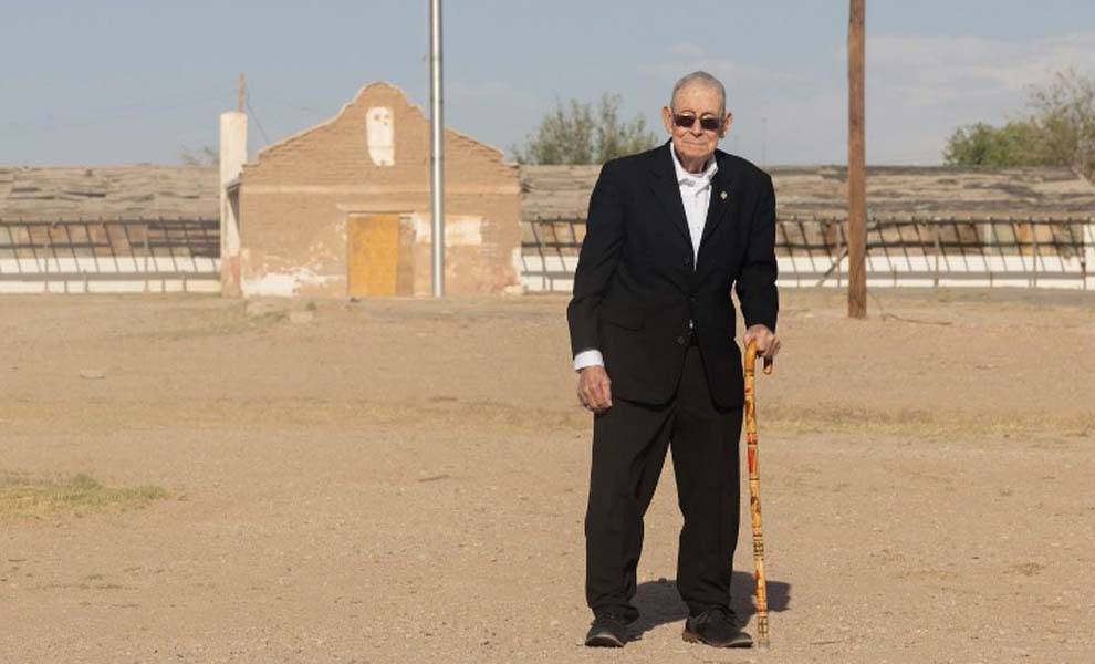 Un hombre mayor con traje y corbata parado frente a un edificio, rezumando profesionalismo y confianza.