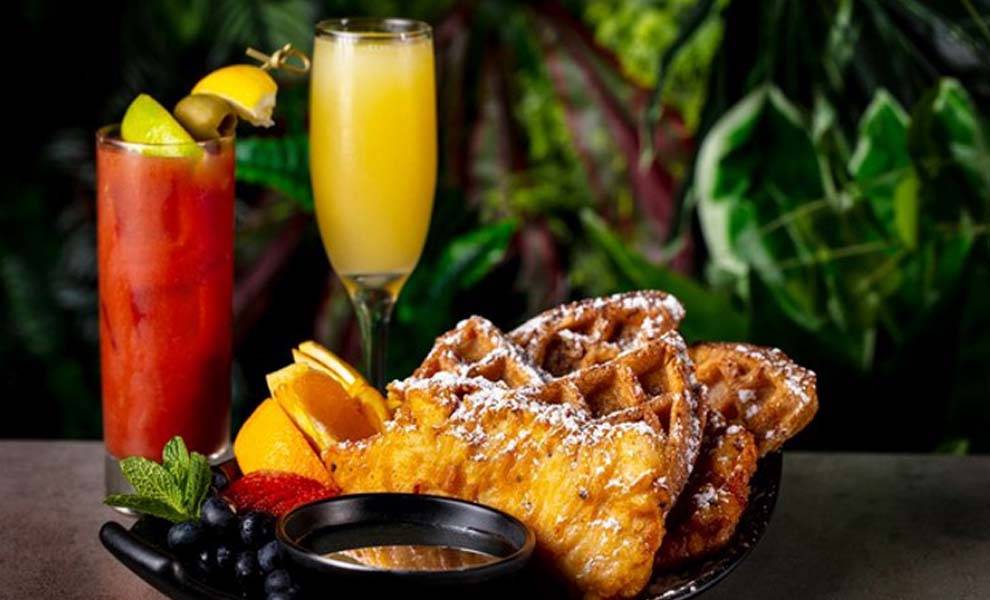 A plate of waffles topped with fruit slices, served with a glass of orange juice