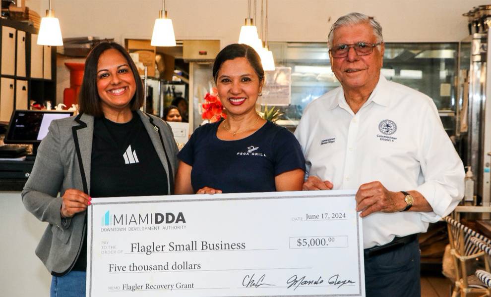Tres personas sonriendo y sosteniendo un cheque con el logotipo de una pequeña empresa, que simboliza el éxito y el apoyo.