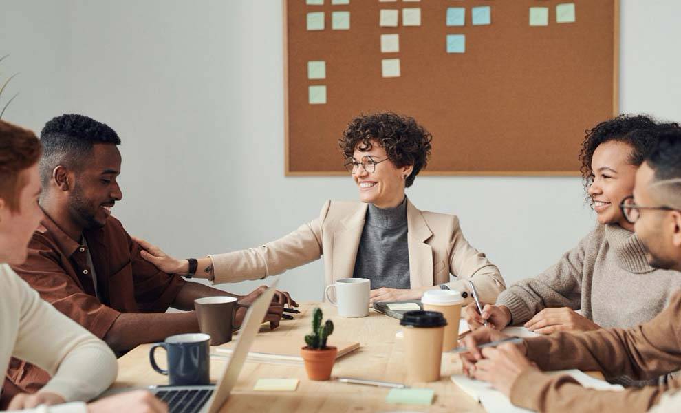 A diverse group of individuals gathered around a table, engrossed in a discussion while using a laptop.