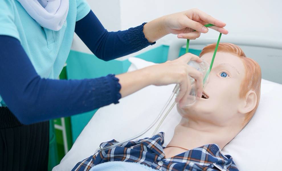Mujer colocando un muñeco en una cama de hospital con fines de formación médica.