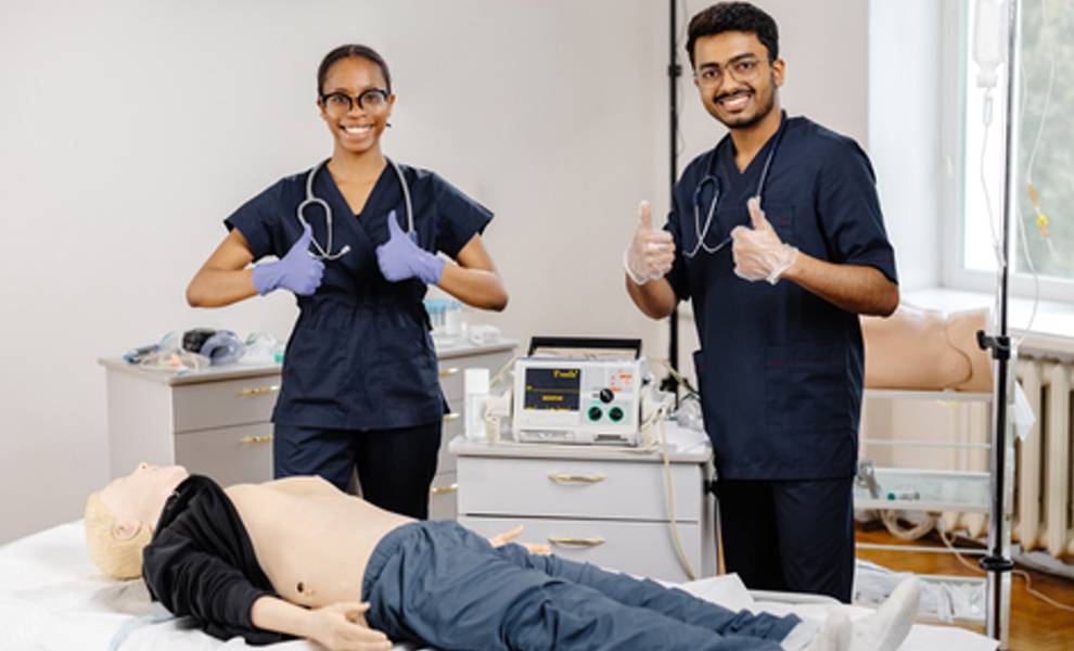 Two MDC nurses training with a mannequin in a hospital room.
